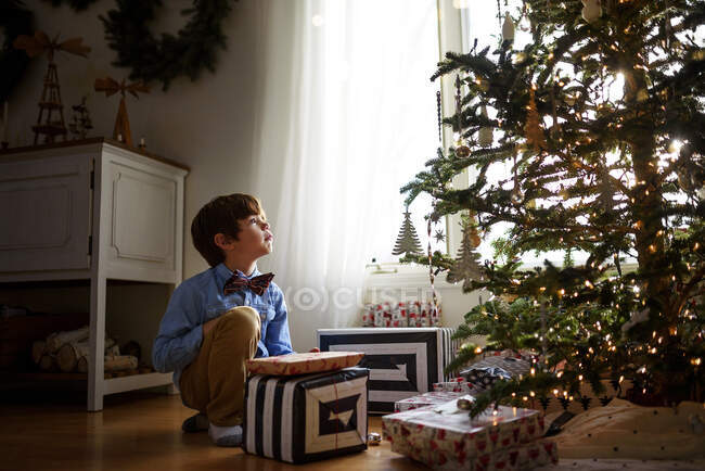 Boy kneeling in front of a Christmas tree with gifts looking up — Stock Photo