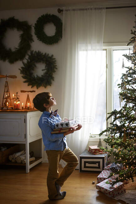 Menino em pé na frente de uma árvore de Natal segurando presentes — Fotografia de Stock