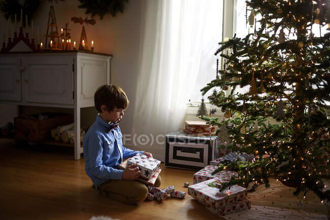Menino sentado na frente de uma árvore de Natal olhando para presentes — Fotografia de Stock
