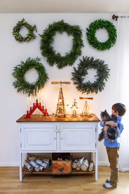 Хлопчик стоїть біля дошки з котом і дивиться на різдвяні прикраси. — стокове фото