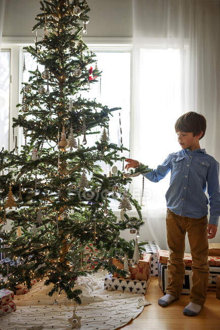Niño de pie frente a un árbol de Navidad - foto de stock
