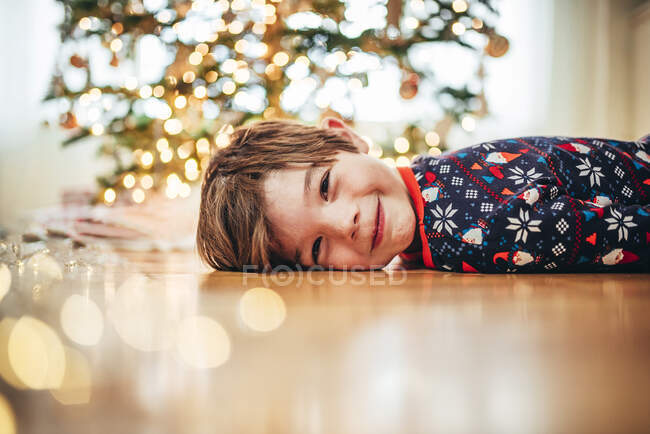 Garçon souriant couché sur le sol devant un sapin de Noël — Photo de stock