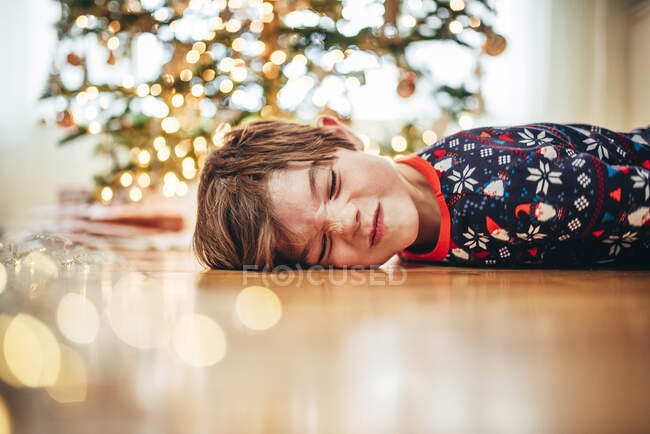Junge liegt auf dem Boden vor Weihnachtsbaum und zieht lustige Gesichter — Stockfoto
