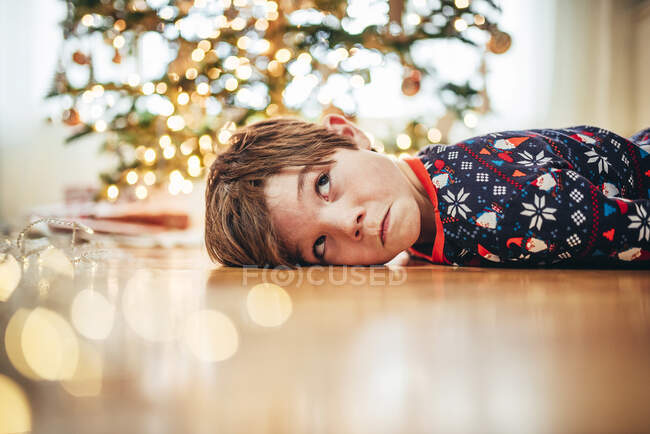 Мальчик лежит на полу перед ёлкой и корчит рожи. — стоковое фото
