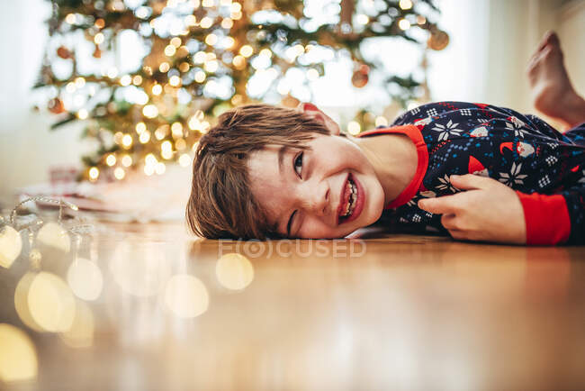 Ragazzo sdraiato sul pavimento davanti a un albero di Natale che ride — Foto stock