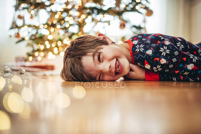 Ragazzo sdraiato sul pavimento davanti a un albero di Natale che ride — Foto stock