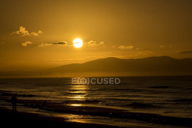 Silhouette of a fisherman on beach at sunrise, Castiglione della Pescaia, Tuscany, Italy — Stock Photo