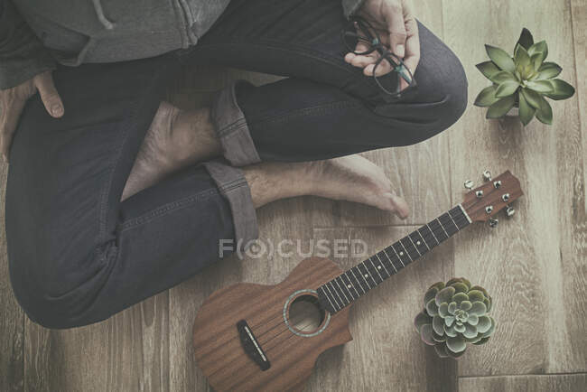 Uomo seduto a gambe incrociate accanto al suo ukulele — Foto stock