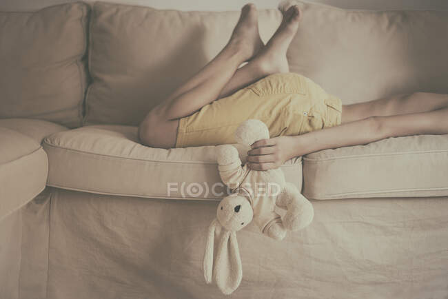 Мальчик лежит на диване с мягкой игрушкой — стоковое фото