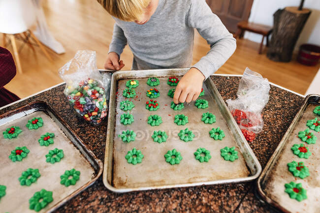 Boy standing in the kitchen decorating cookies — Stock Photo