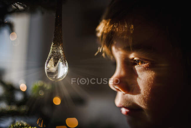 Мальчик смотрит на хрустальный орнамент, висящий на елке — стоковое фото