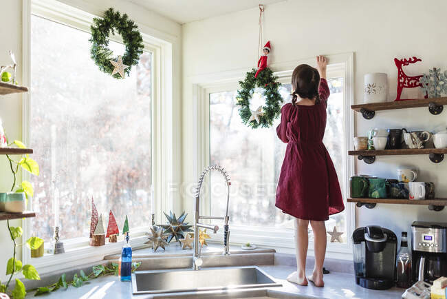 Девушка, стоящая на кухонном столе, раскладывая рождественские украшения — стоковое фото