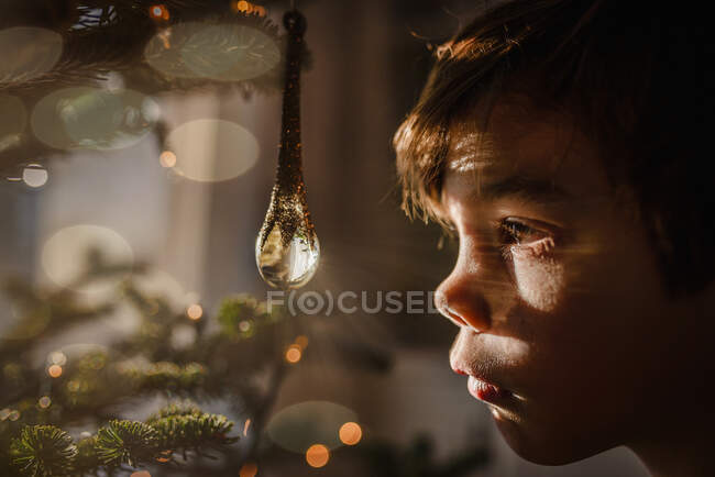 Boy looking at a crystal ornament hanging on a Christmas tree — Stock Photo