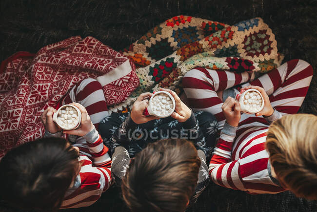 Três crianças sentadas em um sofá bebendo chocolate quente — Fotografia de Stock