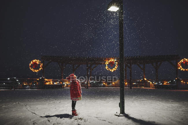 Girl standing in the snow looking up at a street lamp, United States — Stock Photo