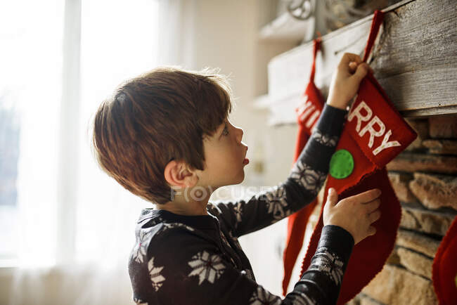 Niño colgando una media de Navidad en una chimenea - foto de stock