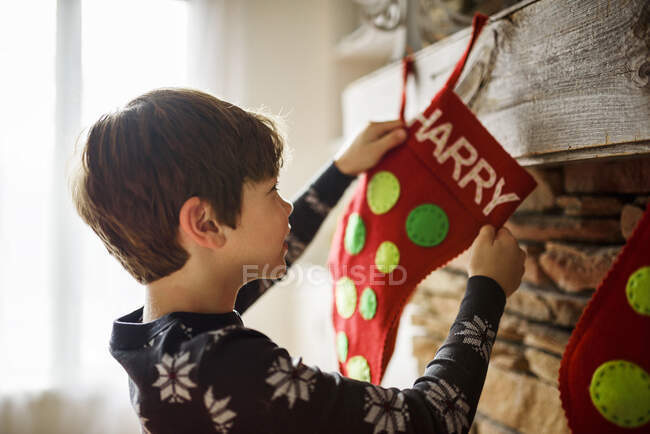 Boy hanging a Christmas stocking on a fireplace — Stock Photo