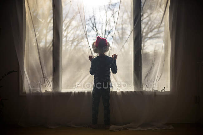 Boy wearing a Santa Hat looking through a window — Stock Photo