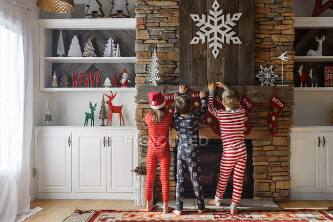 Trois enfants accrochent des bas de Noël sur une cheminée — Photo de stock