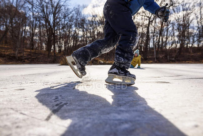 Двоє дітей катаються на ковзанах на замороженому ставку, США. — стокове фото