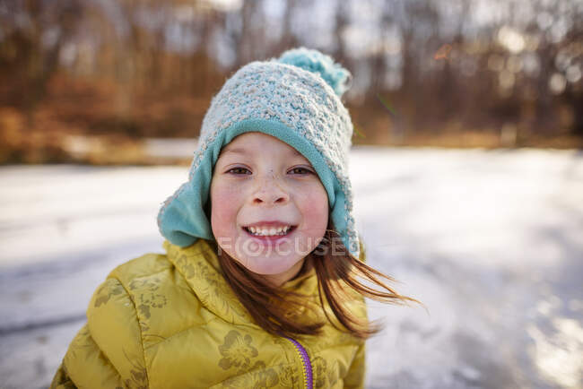 Retrato de una chica sonriente parada junto a un estanque congelado, Estados Unidos - foto de stock
