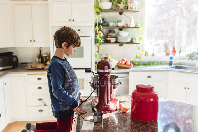 Boy kneeling on stool in the kitchen making a cake — Stock Photo