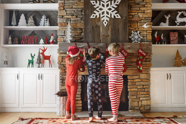 Троє дітей вішають різдвяні панчохи на каміні — стокове фото