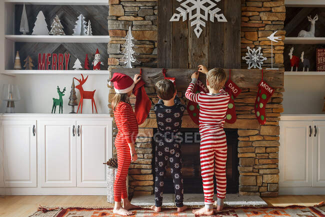 Tre bambini appendere calze di Natale su un camino — Foto stock