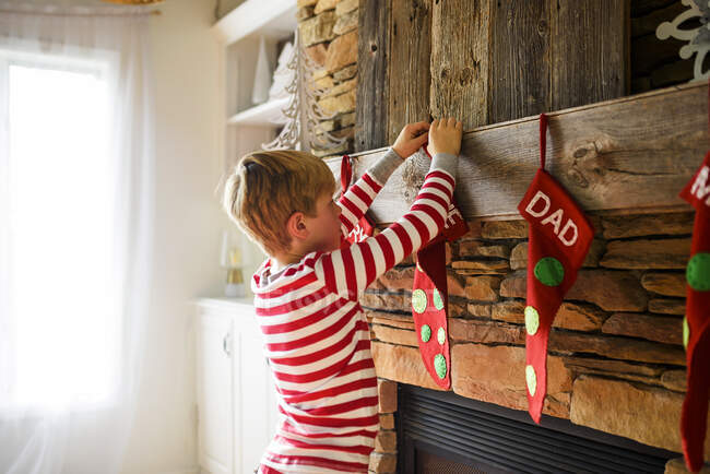 Garçon accrochant un bas de Noël sur une cheminée — Photo de stock