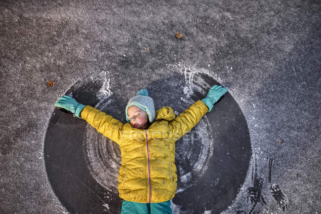 Menina deitada em uma lagoa congelada fazendo um anjo da neve com os braços, Estados Unidos — Fotografia de Stock