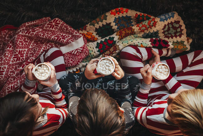 Trois enfants assis sur un canapé buvant du chocolat chaud — Photo de stock