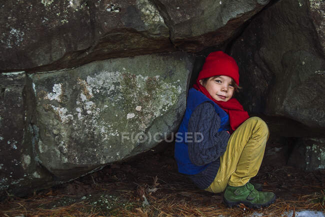 Garçon accroupi dans une forêt par des rochers, États-Unis — Photo de stock
