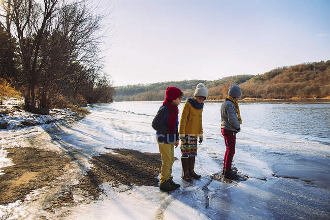 Three children standing at the edge of a frozen lake, United States — Stock Photo