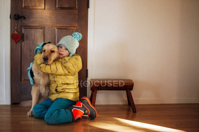 Chica sentada junto a la puerta de su casa abrazando a un perro golden retriever - foto de stock