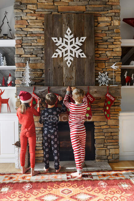 Drei Kinder hängen Weihnachtsstrümpfe am Kamin auf — Stockfoto