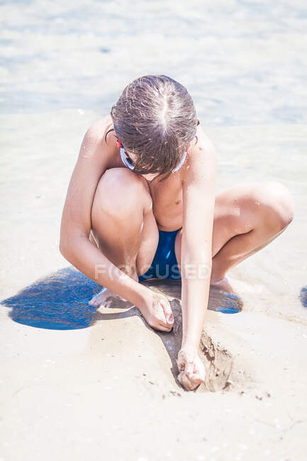 Menino agachado na praia brincando com a areia, Bulgária — Fotografia de Stock