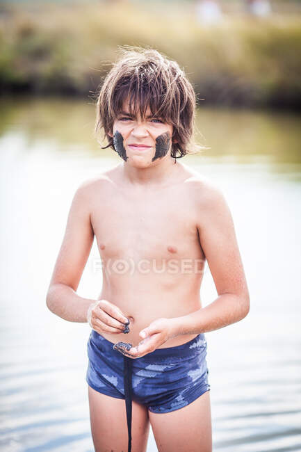 Niño de pie en el lago Atanasovsko poniendo barro en su cara, Burgas, Bulgaria - foto de stock