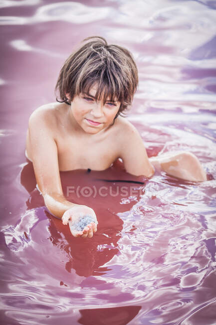 Boy sitting in Atanasovsko Lake holding a handful of salt crystals, Burgas, Bulgaria — Stock Photo