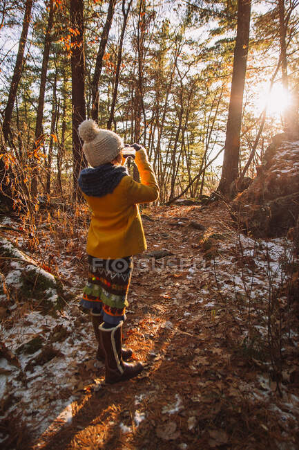 Chica parada en el bosque mirando el sol a través de un pedazo de hielo congelado, Estados Unidos - foto de stock