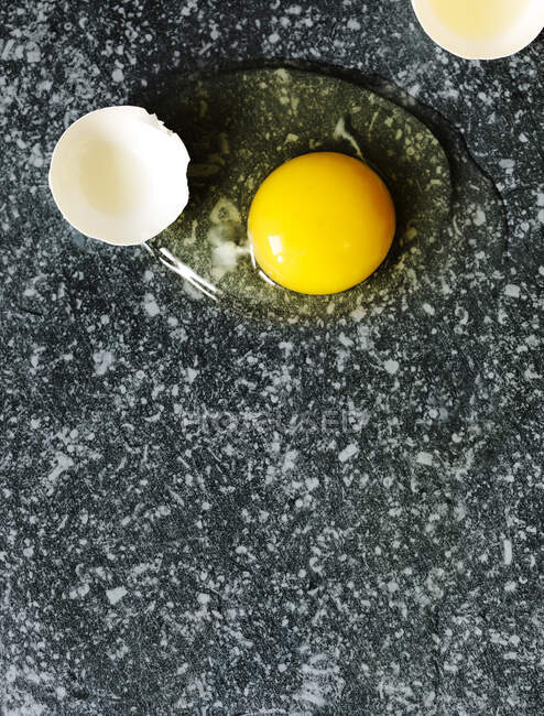 Cracked egg with egg shell, egg yolk and egg white on dark stone background, copy space — Stock Photo