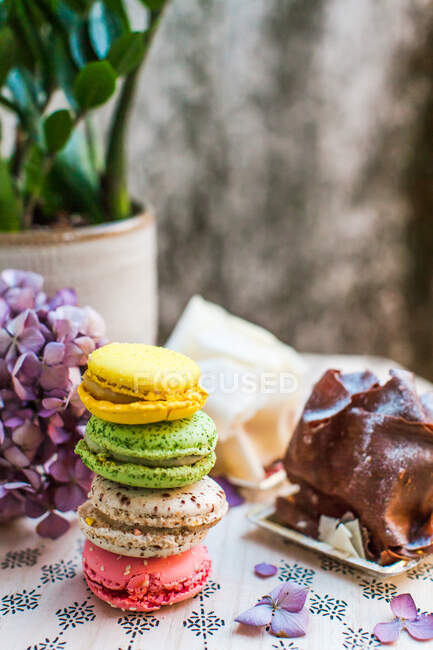 Барвисті солодкі макаруни з десертом і квітами на столі, вид зверху — стокове фото