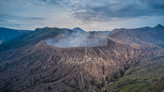 Volcano with smoke in mountainous landscape — Stock Photo