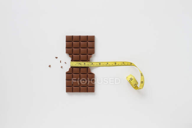 Chocolate bar with a tape measure on a white background. — Stock Photo