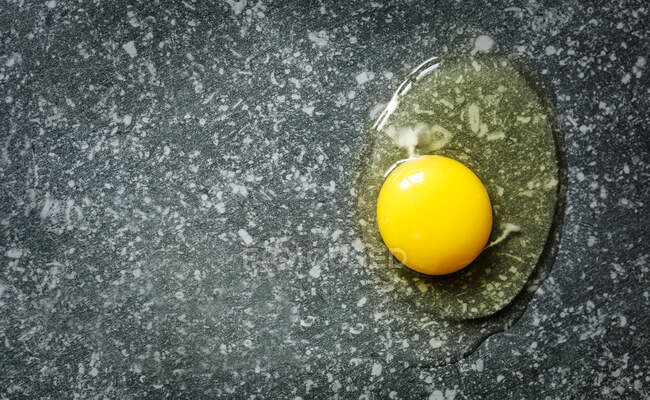 Cracked egg. Egg yolk and egg white on dark stone background, copy space — Stock Photo