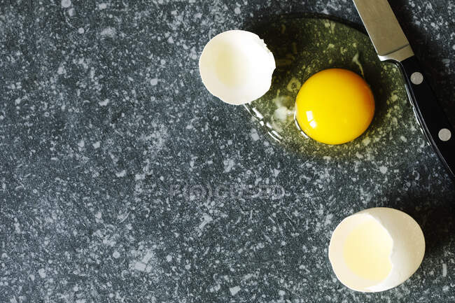 Cracked egg with egg shell, egg yolk and egg white on grey stone background, copy space — Stock Photo
