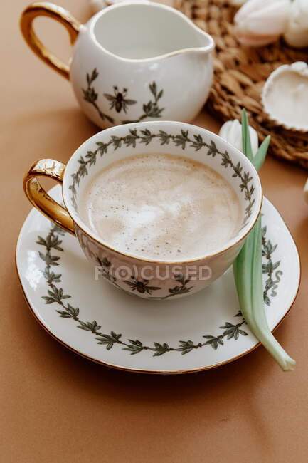 Cup of coffee next to a jug with a tulip on a table — Stock Photo
