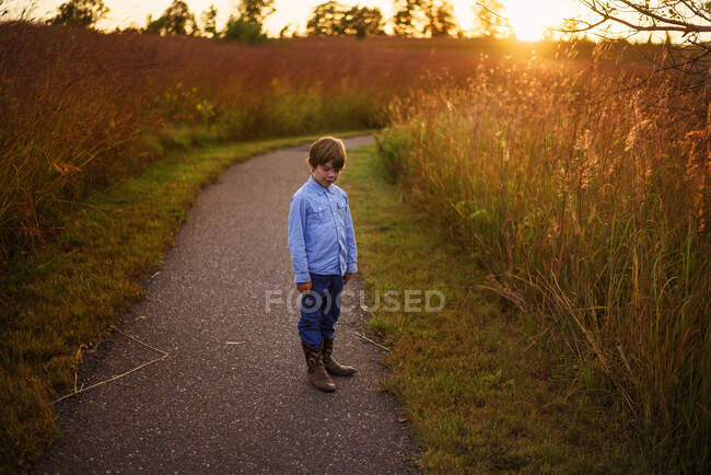 Мальчик, стоящий на тропе у поля на закате, США — стоковое фото