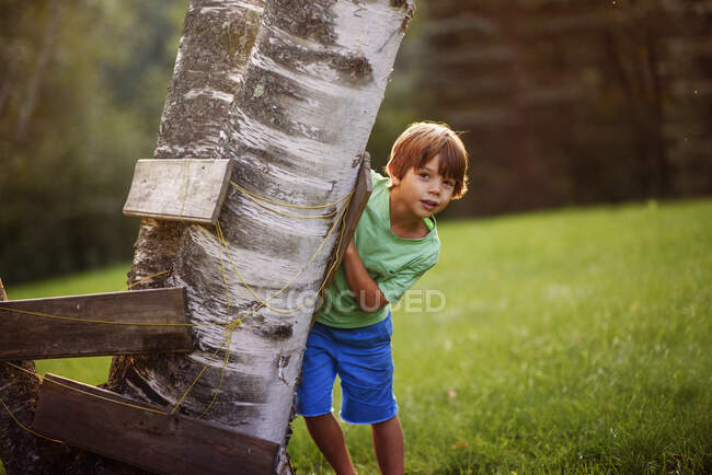 Rapaz escondido atrás de uma árvore forte, Estados Unidos — Fotografia de Stock