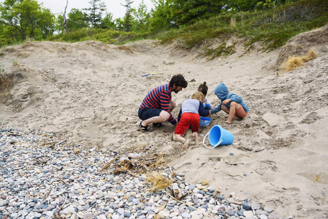 Padre y tres niños construyendo un castillo de arena en la playa, Estados Unidos - foto de stock