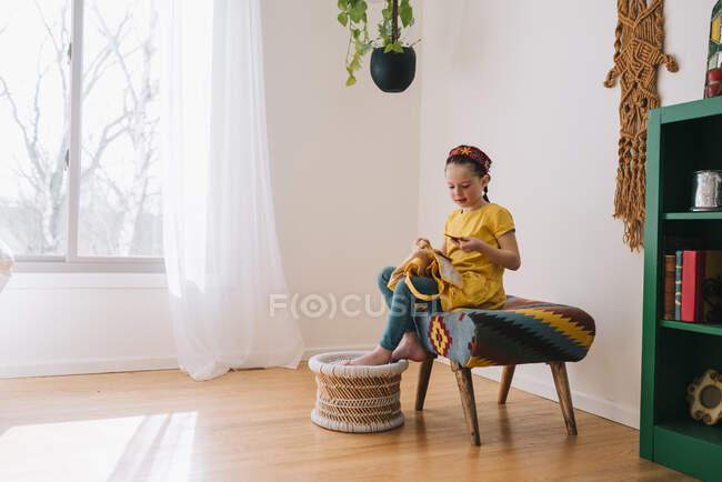 Girl sitting on a stool with her backpack looking at a piece of paper — Stock Photo